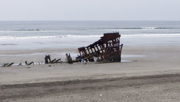 The skeletal bow of the Peter Iredale on the sand at Clatsop Spit, May 2005, visitors beside it for scale